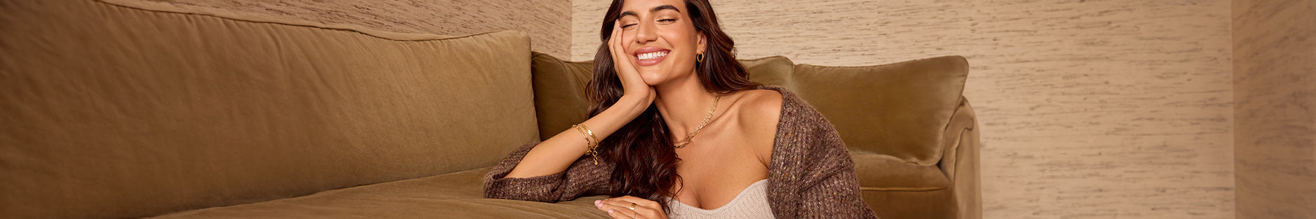 woman against brown couch in gold jewelry